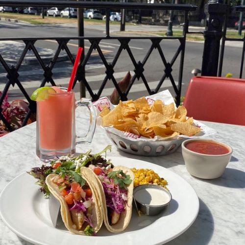A plate of tacos with toppings, a drink, a bowl of chips, and salsa on a table outdoors.