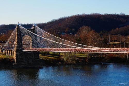 A suspension bridge spans a river, surrounded by autumn trees and hills in the background.