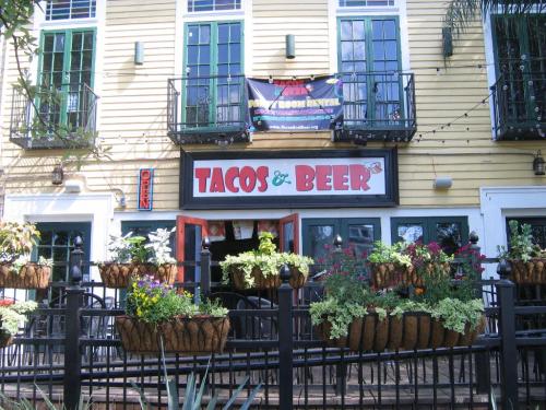 A colorful restaurant exterior featuring a sign that reads "Tacos & Beer," with flower baskets and an open door.