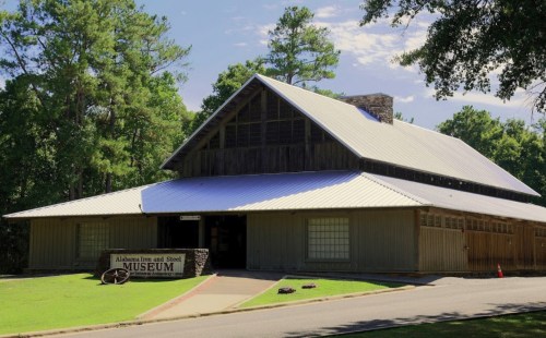 Exterior view of the Alabama Iron and Steel Museum, featuring a wooden structure and a metal roof surrounded by trees.