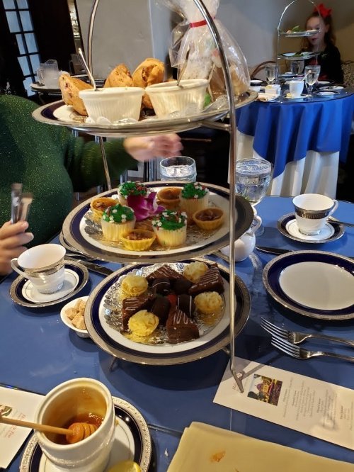 A tiered stand with assorted pastries, cupcakes, and snacks, set on a table with tea and elegant tableware.
