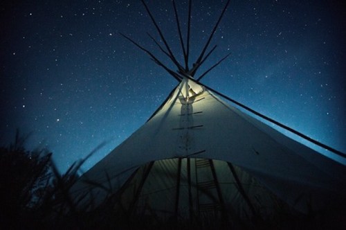 A teepee illuminated from within, set against a starry night sky.