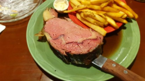 A plate featuring a large slice of prime rib with a side of golden fries and a small dish of butter.