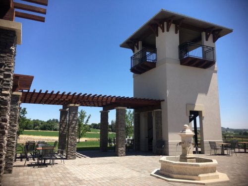 A modern building with a tower, surrounded by stone columns and a fountain, set against a clear blue sky.