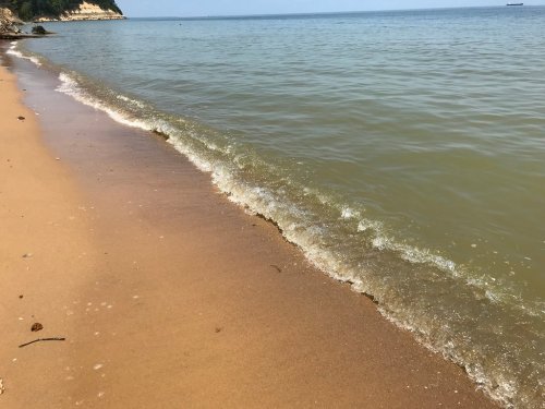 A sandy beach with gentle waves lapping at the shore under a clear blue sky.