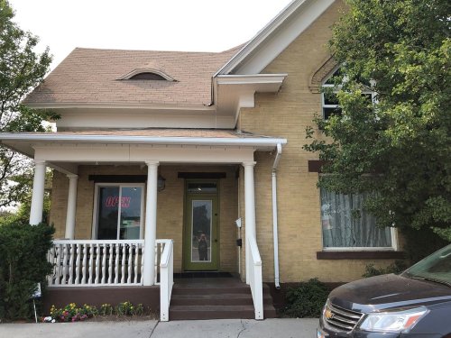 A yellow brick house with a porch, open sign, and greenery around it, showcasing a welcoming entrance.