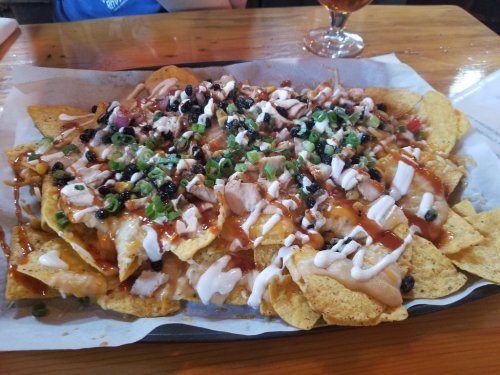 A large plate of nachos topped with chicken, black beans, green onions, and drizzled with barbecue sauce and sour cream.
