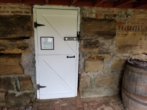 A white wooden door with a latch, set in a stone wall, next to a wooden barrel.