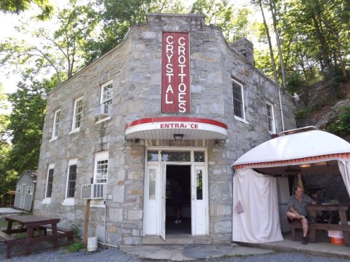 A stone building with a sign reading "Crystal Grottoes" and a man sitting outside under a canopy.