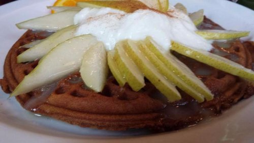 A waffle topped with sliced pears, whipped cream, and a drizzle of syrup, served on a white plate.
