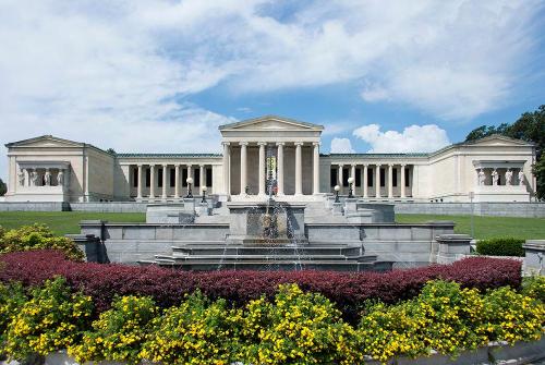 A grand museum building with classical architecture, surrounded by lush greenery and colorful flower beds.