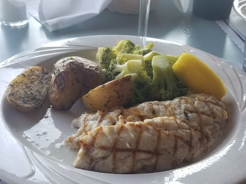 Grilled fish fillet served with roasted potatoes, steamed broccoli, and a lemon wedge on a white plate.