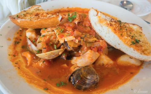A bowl of seafood stew with shrimp, clams, and vegetables, served with two slices of toasted garlic bread.