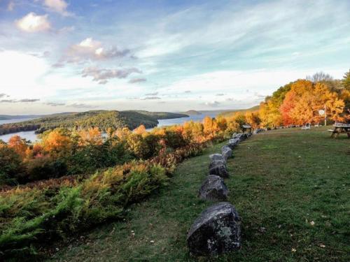 Scenic view of a lake surrounded by colorful autumn foliage and rolling hills under a partly cloudy sky.