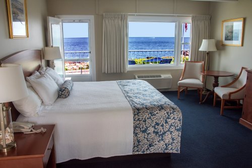 Cozy hotel room with a king bed, seating area, and ocean view through large windows.