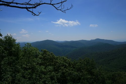 A panoramic view of lush green mountains under a clear blue sky with a few clouds.
