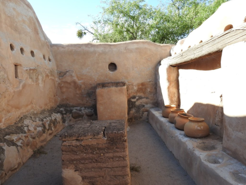 Interior of an ancient adobe structure with clay pots and a stone bench, surrounded by earthy walls and natural light.