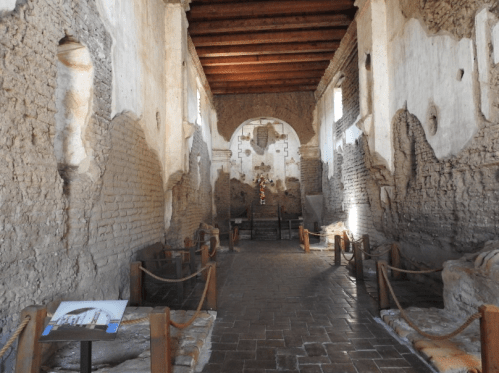 Interior of an ancient stone building with exposed walls, wooden beams, and a small altar at the far end.