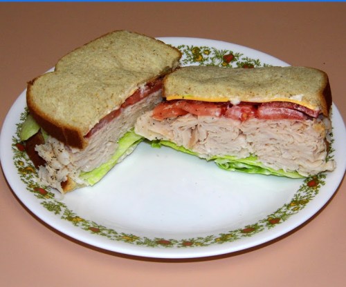 A sandwich with turkey, lettuce, tomato, and mayonnaise on whole grain bread, served on a decorative plate.