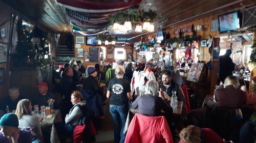 A busy rustic restaurant filled with people dining and socializing, decorated with flags and memorabilia.
