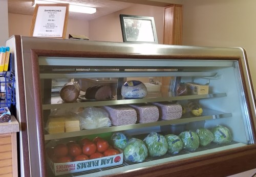 A display case filled with various meats, cheeses, and fresh produce, with a menu sign on top.