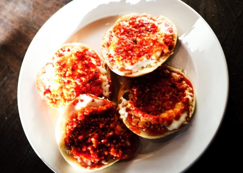 Four round pastries topped with red sauce and chopped ingredients, served on a white plate.
