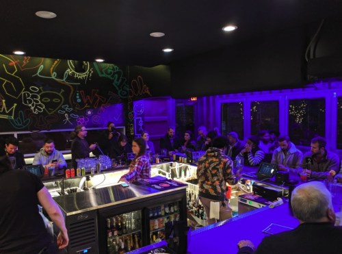 A lively bar scene with patrons socializing, colorful graffiti on the walls, and a bartender serving drinks.