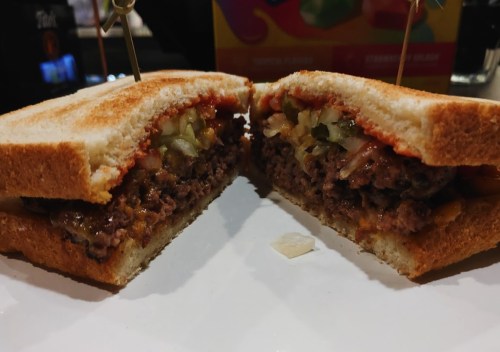 A cross-section of a sandwich with a beef patty, toppings, and ketchup between two slices of white bread.