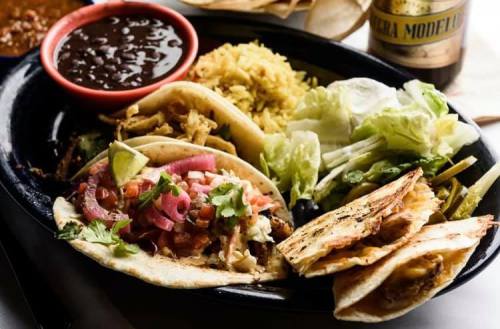 A vibrant plate of tacos with toppings, rice, black beans, and fresh lettuce, accompanied by a bottle of beer.