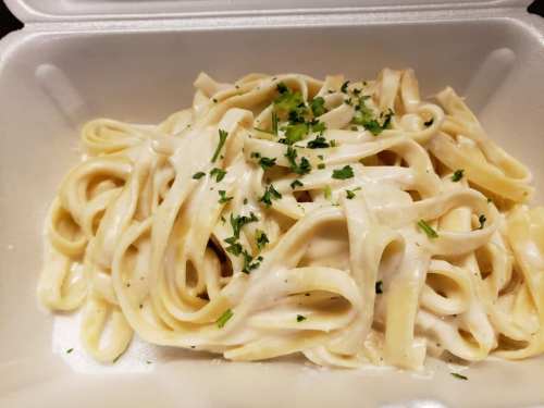 Creamy fettuccine pasta topped with fresh parsley in a takeout container.