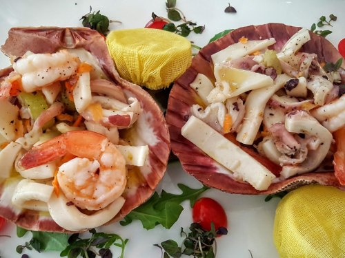 Two scallop shells filled with a seafood salad, featuring shrimp, squid, and colorful vegetables, garnished with herbs.