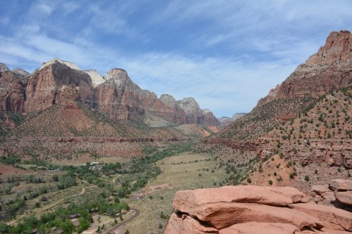 A panoramic view of Zion National Park, showcasing red rock formations and lush green valleys under a blue sky.