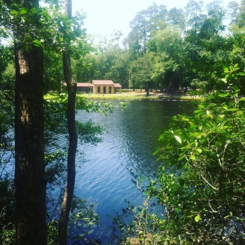 A serene lake surrounded by trees, with a small building visible on the shore in a peaceful natural setting.