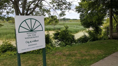 Sign reading "Window on the Waterfront" beside a lush green area with water and tall grasses in the background.