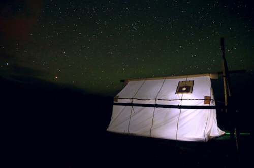 A white tent illuminated at night, surrounded by a starry sky.