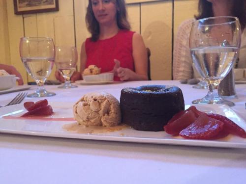A dessert plate featuring a chocolate cake, ice cream, and fruit garnishes, with diners in the background.