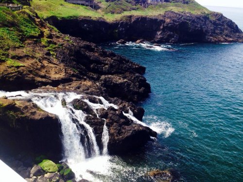 A scenic view of a rocky coastline with a small waterfall cascading into the blue ocean.