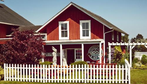 A red barn-style café with white trim, surrounded by a white picket fence and colorful outdoor seating.