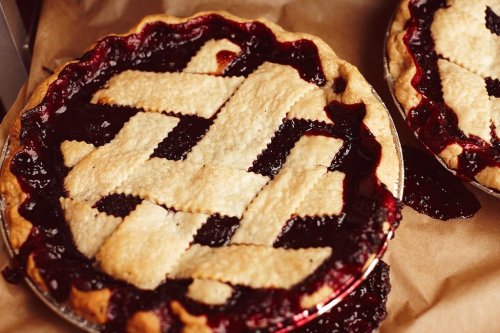 Two freshly baked berry pies with a golden lattice crust, resting on parchment paper.