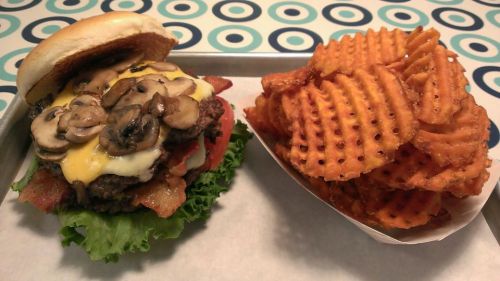 A juicy burger topped with mushrooms, cheese, and bacon, served with a side of crispy waffle fries.
