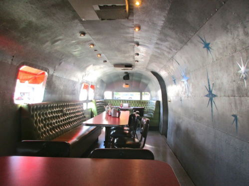 Interior of a retro diner with metallic walls, green booths, and red tables, featuring star-shaped decorations.