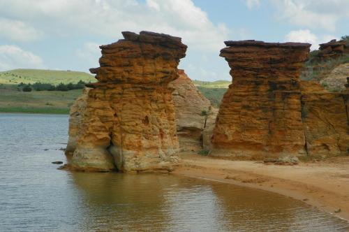 Two tall, rocky formations rise from the water's edge, surrounded by a serene landscape and blue sky.
