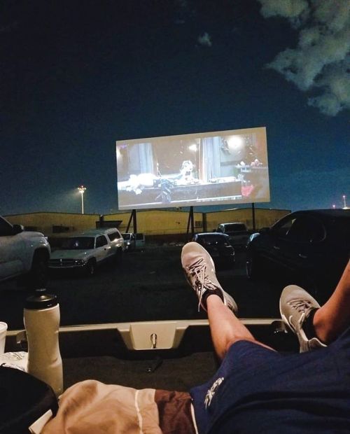 A person relaxes in a truck bed, watching a movie on a large outdoor screen at night.