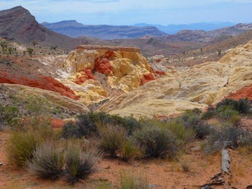 A colorful desert landscape featuring layered rock formations in shades of red, orange, and yellow, surrounded by sparse vegetation.