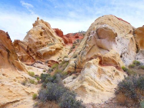Colorful rock formations with smooth curves and textures, surrounded by sparse vegetation under a blue sky.