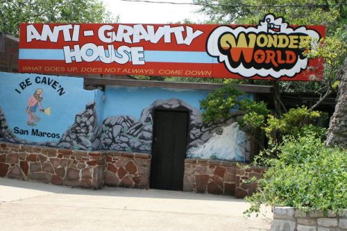 Sign for "Anti-Gravity House" at Wonder World, featuring colorful graphics and a cave mural on the wall.