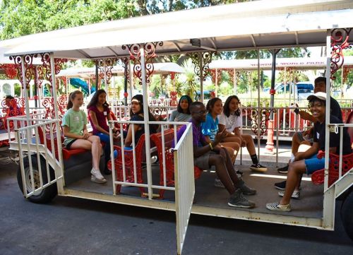 A group of children sitting on a colorful tram in a park, smiling and enjoying their time together.