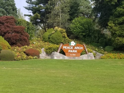 Sign for Peace Arch Park surrounded by colorful flowers and lush greenery.