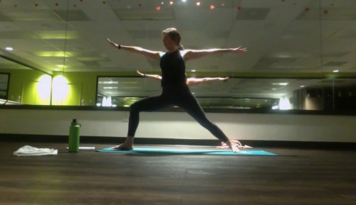 A person practicing yoga in a warrior pose on a mat, with a mirrored background and soft lighting.