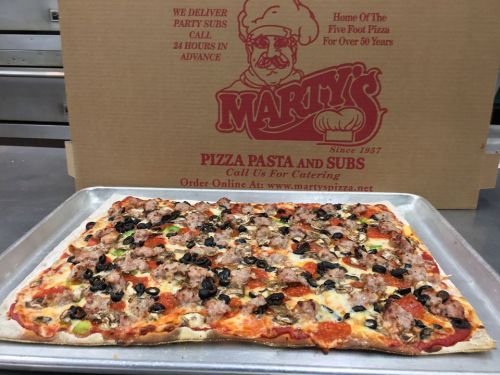 A freshly baked pizza topped with sausage, pepperoni, olives, and vegetables on a tray, with a pizza box in the background.